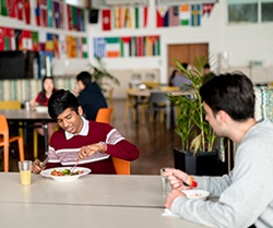 Image of two students seated at a table in the dining hall eating lunch and talking
