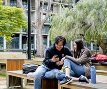 Image of students talking together and looking at a students phone in the outdoor quadrangle