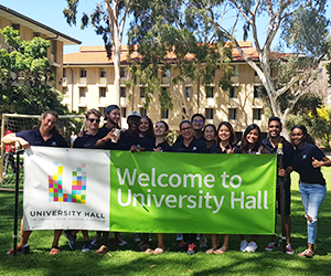 Image of students standing at a welcome to university hall sign in the upper quad