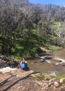 Image of Hamed sitting on a river bank on a hike