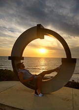 Image of Hamed sitting by a statue on the coast