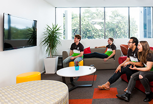 UniHallers in a common area with TV, couches, view of UWA, table, laptops all laughing together